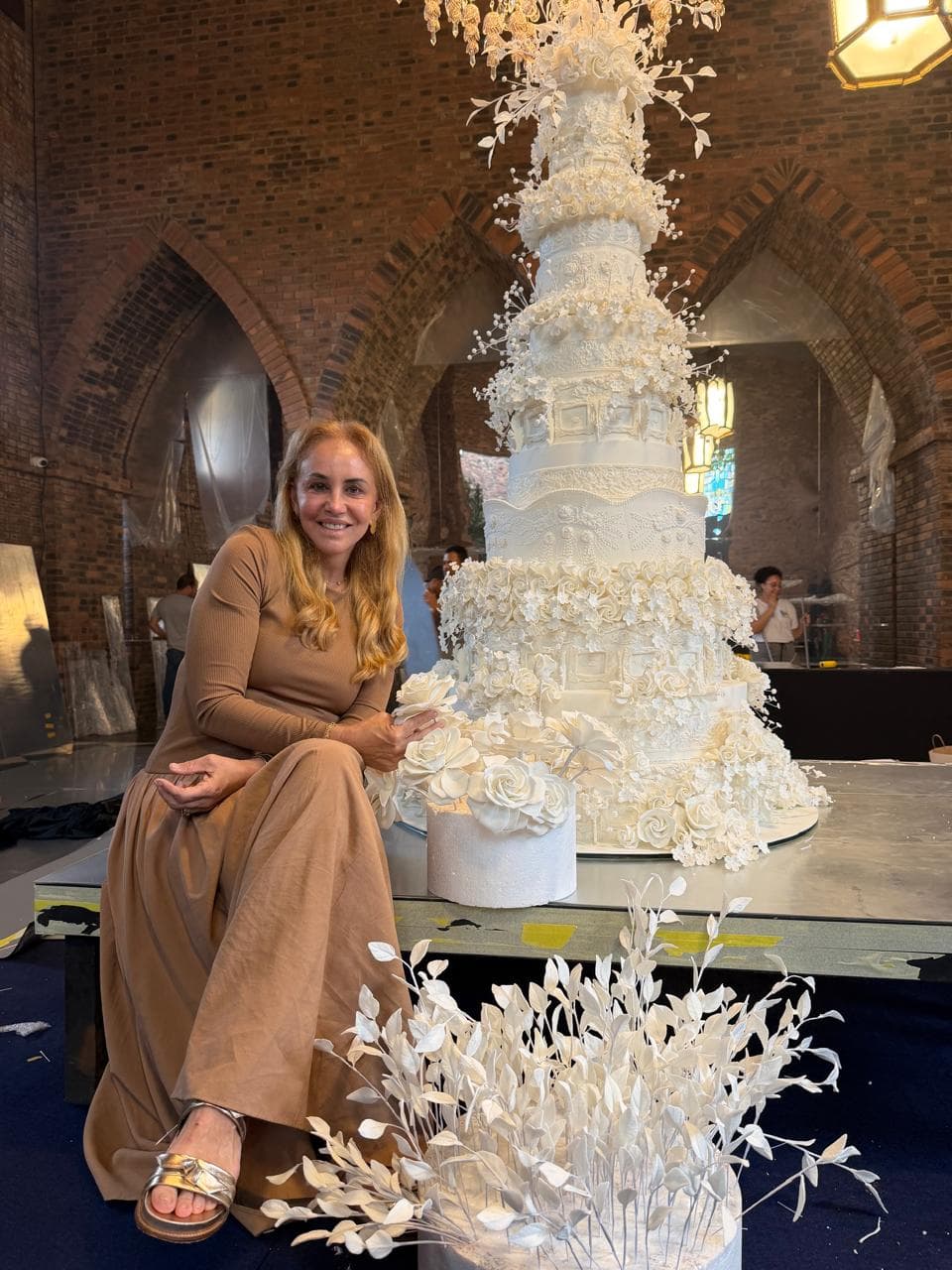Lucinha Cascão ao lado de um bolo de casamento feito pelo ateliê